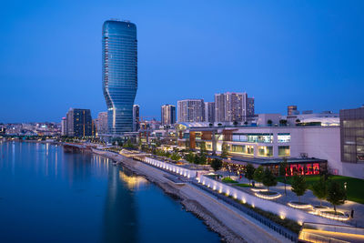 Buildings by river against clear blue sky