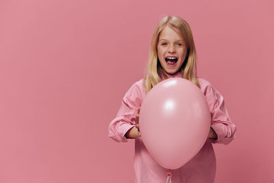 Portrait of young woman holding balloons against pink background