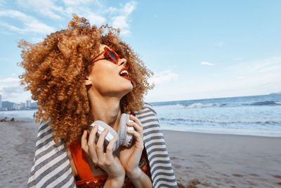 Young woman using mobile phone while standing at beach against sky