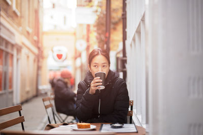 Full length of man holding coffee while sitting on table at cafe