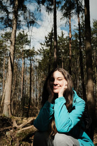 Portrait of smiling young woman sitting on tree trunk in forest