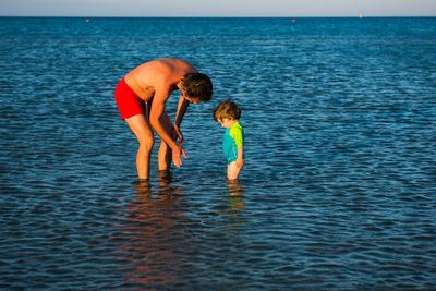 Father and daughter standing in sea against sky
