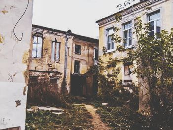 Old abandoned house by building against sky