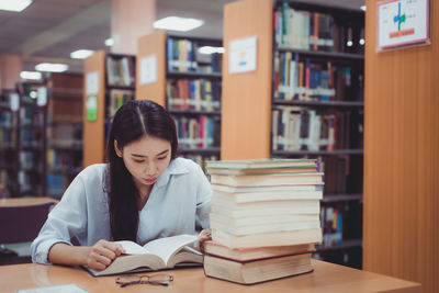 Thoughtful woman reading book in library 