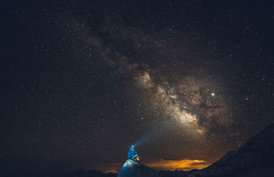 Low angle view of man sitting on cliff against milk way in sky at night