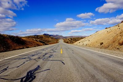 Empty road leading towards mountain against sky