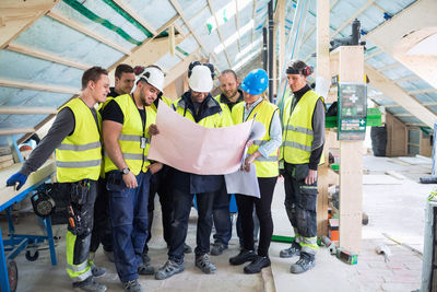 Manager standing with manual workers while reading blue prints at construction site