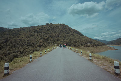 Rear view of people walking on road amidst mountains against sky
