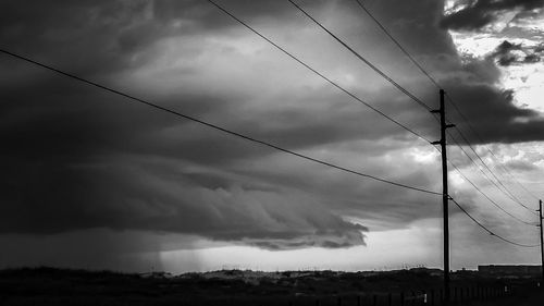 Low angle view of electricity pylon against cloudy sky