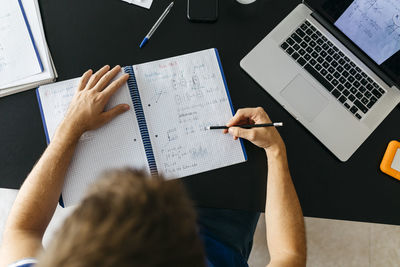 Male student solving mathematical equations in workbook while sitting at table