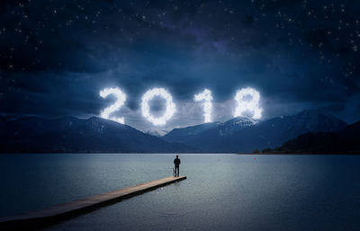 Man standing on pier over river against illuminated number