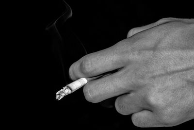 Cropped image of hand holding cigarette against black background