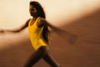 Artistic speed blur of young woman running against yellow wall