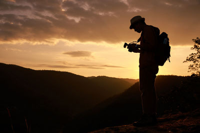 Silhouette man photographing on mountain against sky during sunset