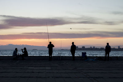 Silhouette people on beach against sky during sunset