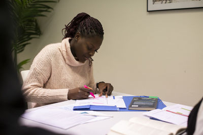 Portrait of female student using highlighter on paper while sitting in classroom