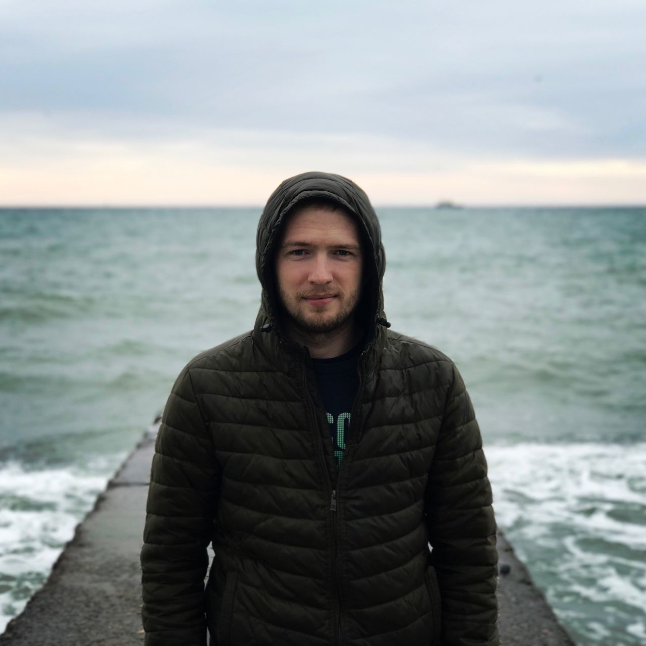 portrait, looking at camera, sea, front view, sky, beard, lifestyles, young adult, standing, men, real people, one person, beach, only men, water, confidence, one man only, horizon over water, outdoors, nature, day, wave, adult, adults only, people