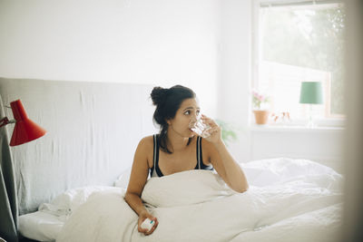 Young woman looking away while sitting on bed at home