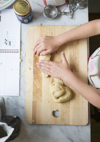 Cropped image of girl making dough on cutting board at kitchen