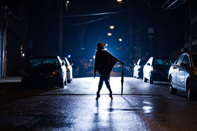 Rear view of woman with umbrella standing on street at night