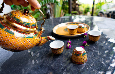 Close-up of hand pouring water from teapot in cup over table