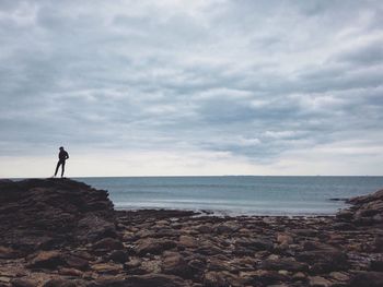 Man on rocky shore against sky