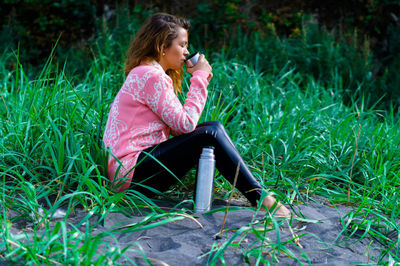 Full length of woman drinking water while sitting on grass