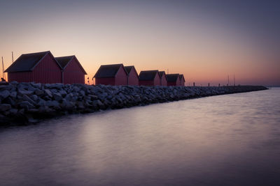 Beach huts on groyne in sea against sky during sunset