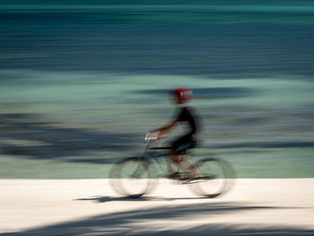 Blurred motion of man riding bicycle on road