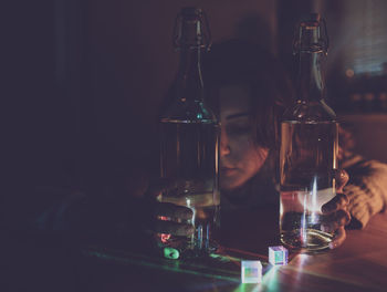 Thoughtful woman with wine bottles on table in darkroom