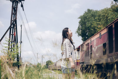 Side view of smiling woman standing on land by train against sky