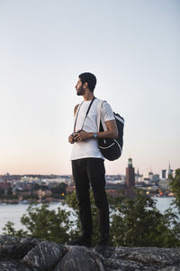 Male tourist looking at view while standing on rock against clear sky