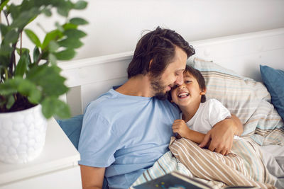 Dad reads a book lying in a white bed to his son child before going to bed