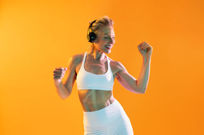 Portrait of young woman with arms raised standing against yellow background
