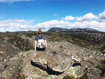Rear view of man sitting on rock against sky