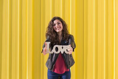 Portrait of smiling woman standing against yellow wall