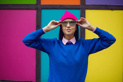 Fashionable brunette woman in a pink warm hat and sweater and sunglasses stands against background