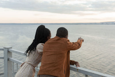 Young couple standing by railing looking at river