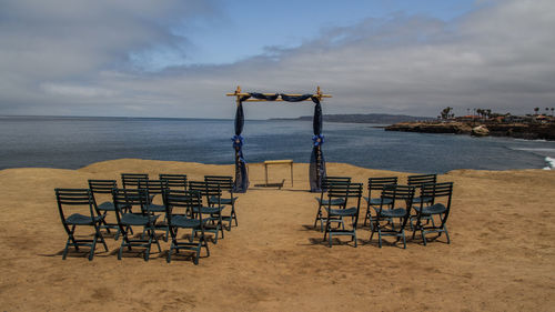 Empty chairs and table on beach against sky