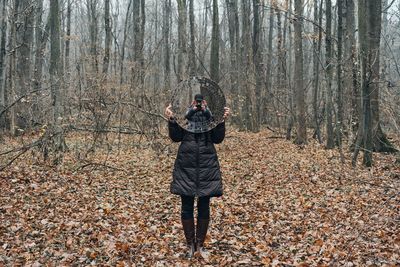 Woman holding mirror with reflection while standing on field in forest
