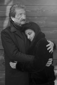 Senior couple embracing while standing against wood