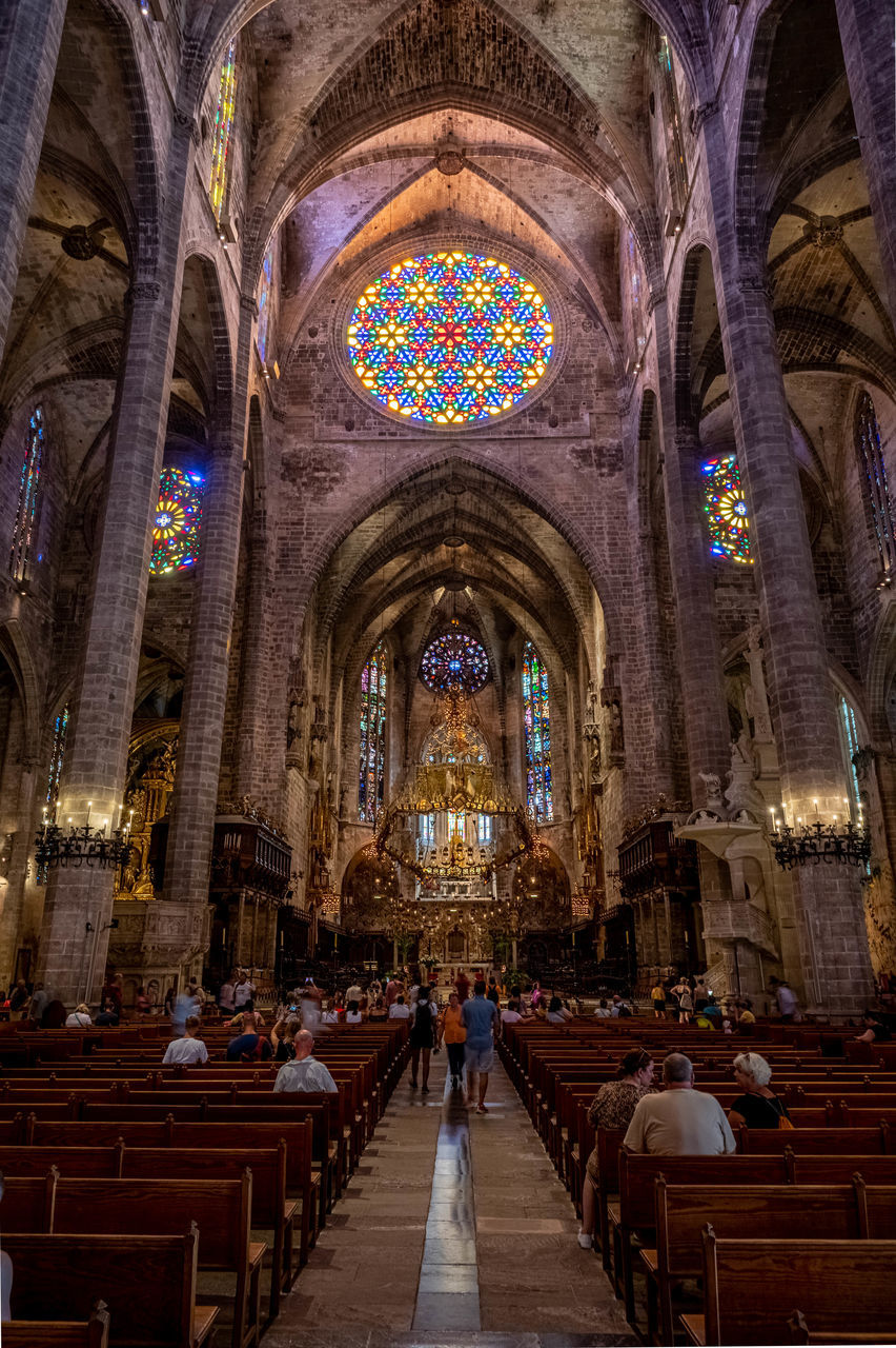 architecture, religion, place of worship, belief, spirituality, built structure, building, catholicism, indoors, travel destinations, arch, pew, worship, travel, history, stained glass, tourism, the past, glass, altar, praying, seat, window, adult, group of people, ceiling, bench, aisle, tourist