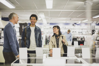 Mature owner talking to smiling male and female customers in electronics store