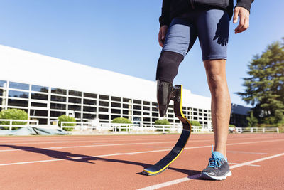 Low section of athlete with prosthetic leg standing on running track