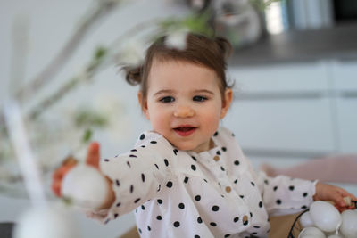 A little girl sits on a table and decorates spring branches with easter eggs.