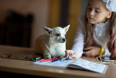 Cute girl reading by dog sitting on table at home 