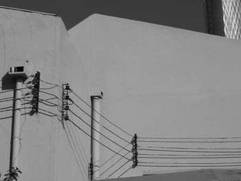 Low angle view of electricity pylon by building against sky