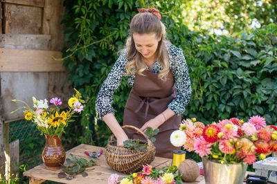 Cute florist girl collects a bouquet of autumn flowers in a basket on the table