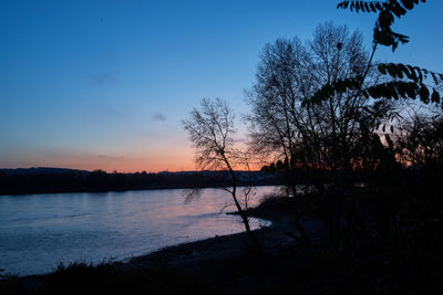 Silhouette trees by lake against sky at sunset