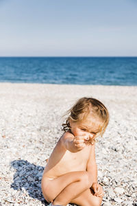 Naked girl crouching on rocks at beach during sunny day